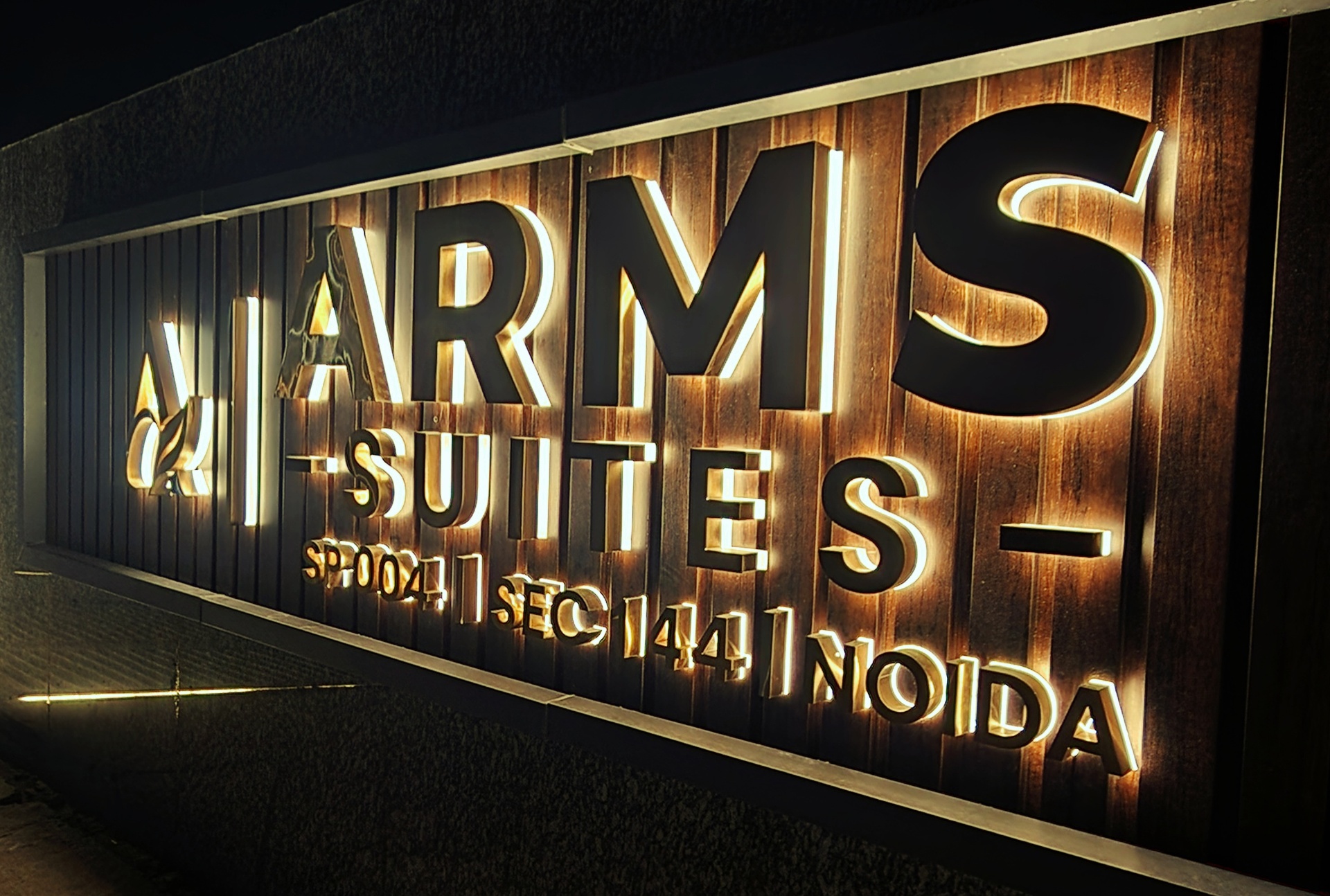 Illuminated ARMS Suites signage at night — boutique hotel branding